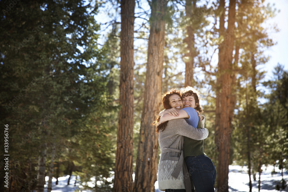 Cheerful friends hugging while standing in forest during winter Cheerful friends hugging while standing in forest during winter