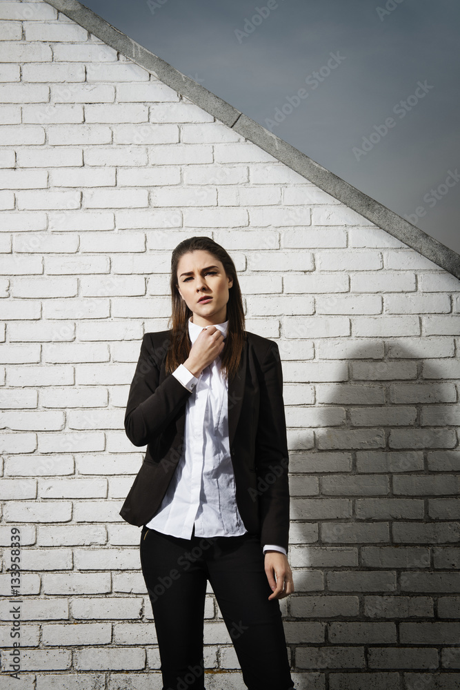 Portrait of confident businesswoman adjusting collar while standing against brick wall Portrait of confident businesswoman adjusting collar while standing against brick wall