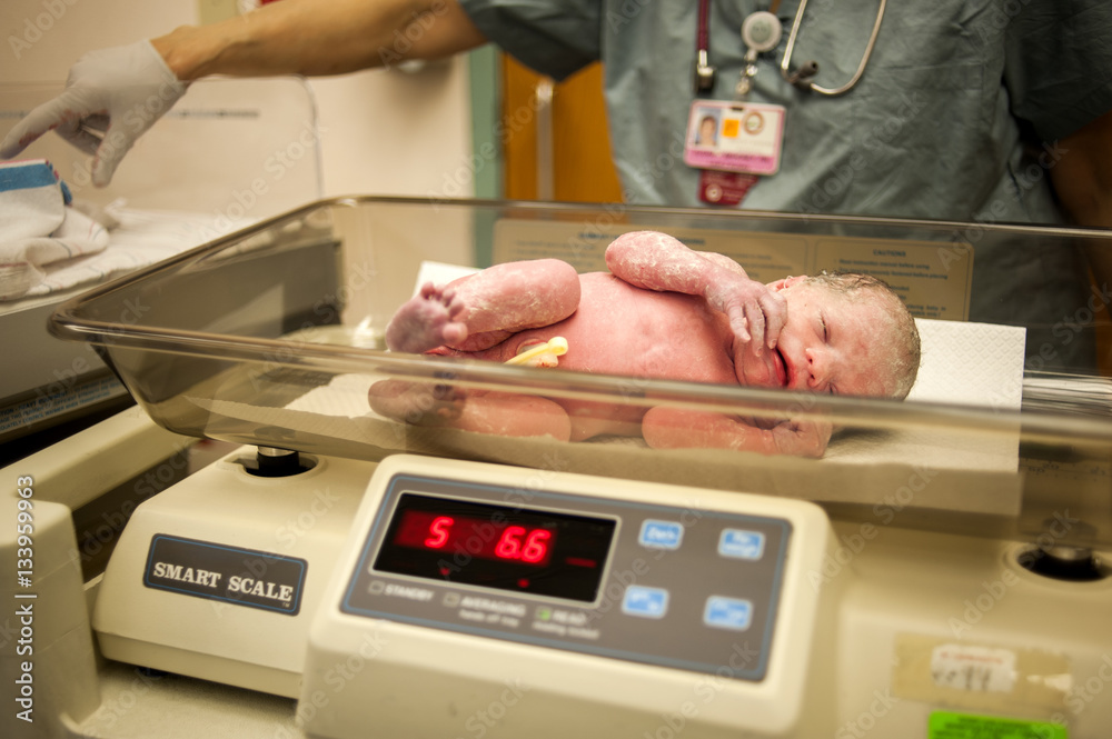 Newborn baby on weight scale in hospital Stock Photo
