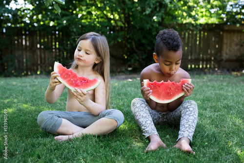 Children eating watermelon slices while sitting on the grass photo
