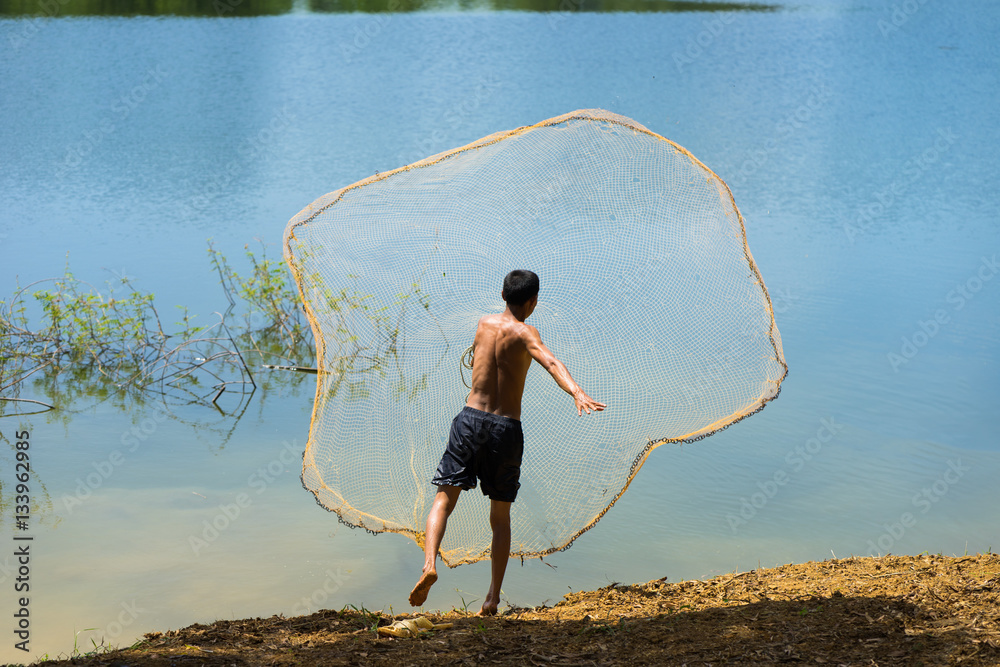 Back view of Asian fisherman throwing fish net to catch fish on