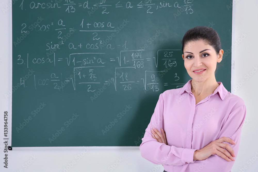 Young female teacher beside blackboard on white background