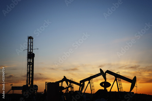 Silhouette oil pumps on field against sky during sunset
