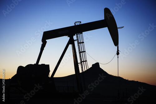 Silhouette oil pump on field against sky during sunset