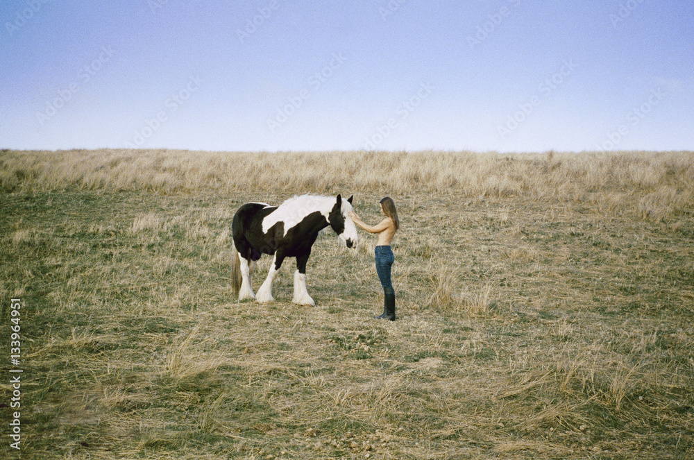 Side view of topless woman stroking horse on grassy field against clear sky Side view of topless woman stroking horse on grassy field against clear sky