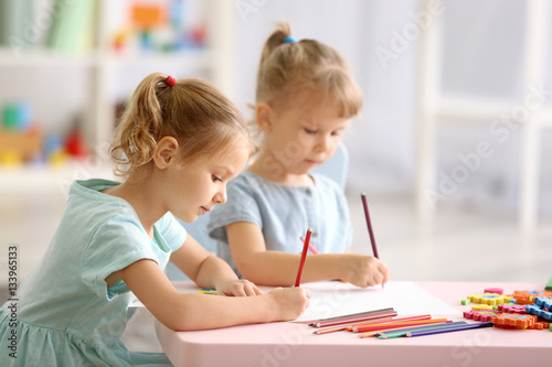 Adorable little sisters drawing and sitting at table