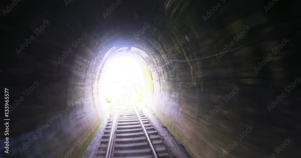 Abstract video of fast moving camera through old railway tunnel toward bright light