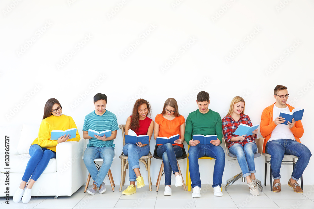 Obraz premium Group of people reading books while sitting near light wall