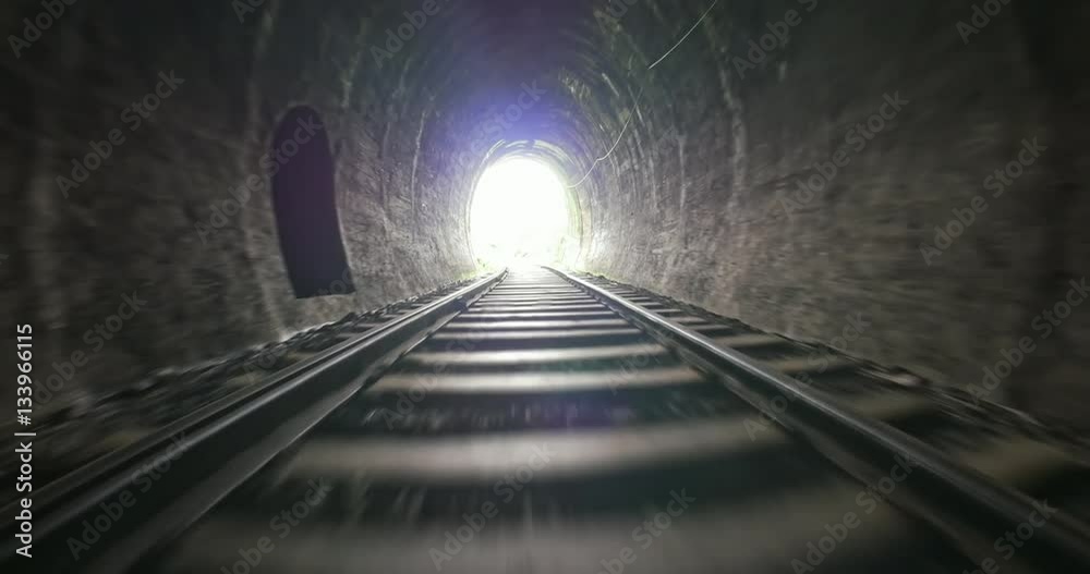 Fast moving camera in dark old railway tunnel toward bright light in the end