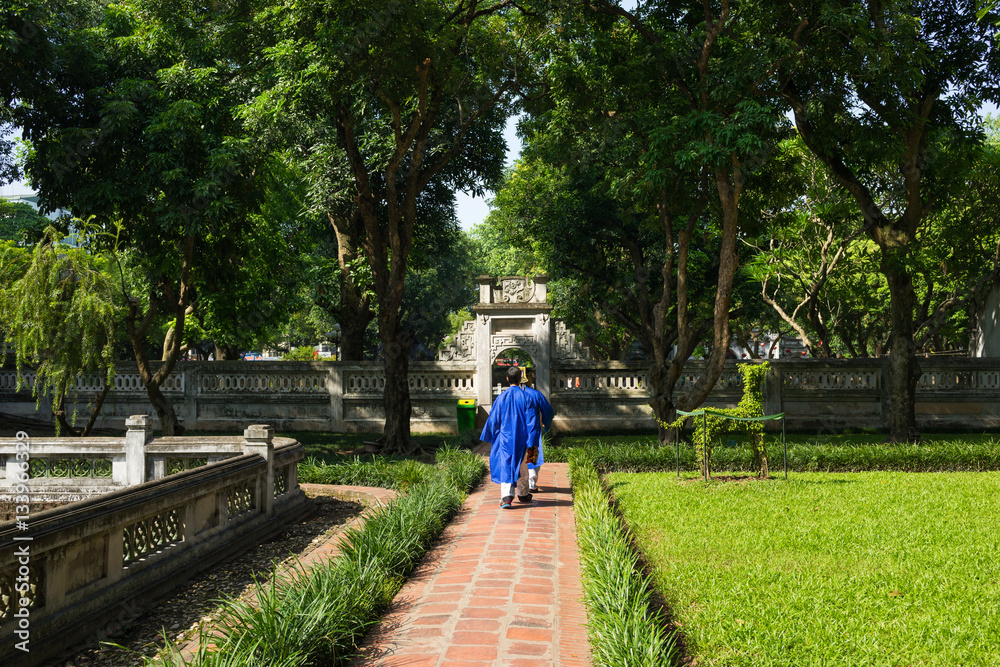 Second courtyard in Temper of Literature ( Van Mieu ) with two men wearing old traditional long dress Ao Dai walking on courtyard