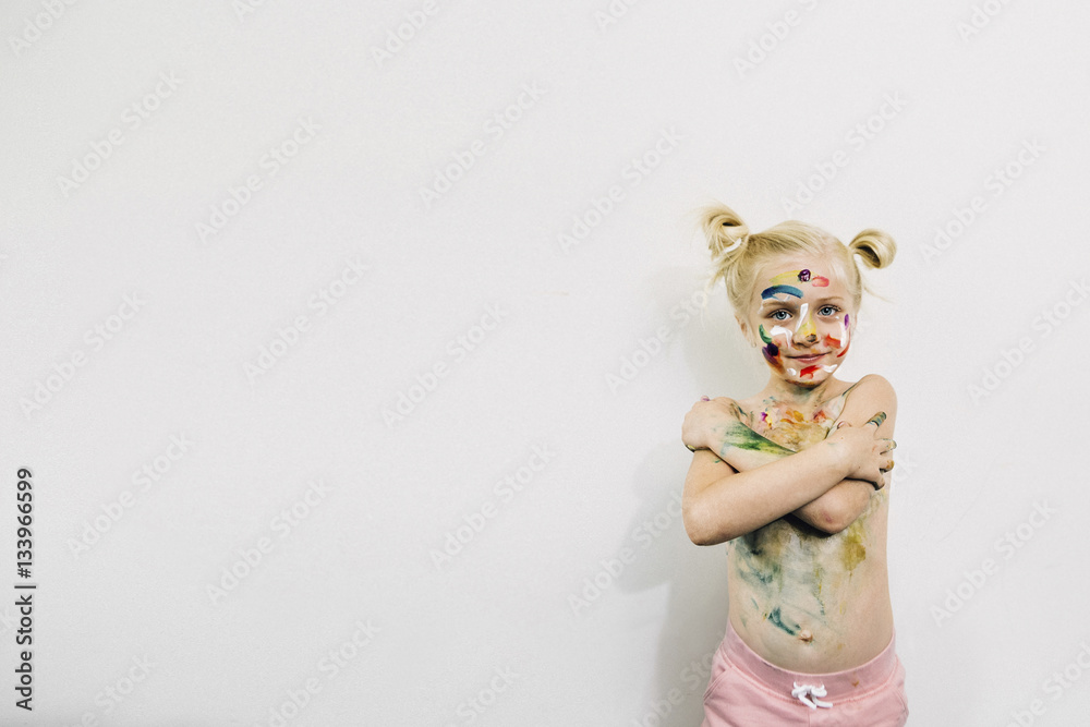 Cute girl covered in messy paint standing against white wall Cute girl covered in messy paint standing against white wall