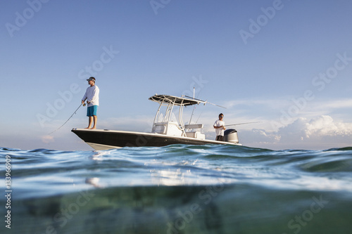 Low angle view of men fishing while standing on boat at sea against sky