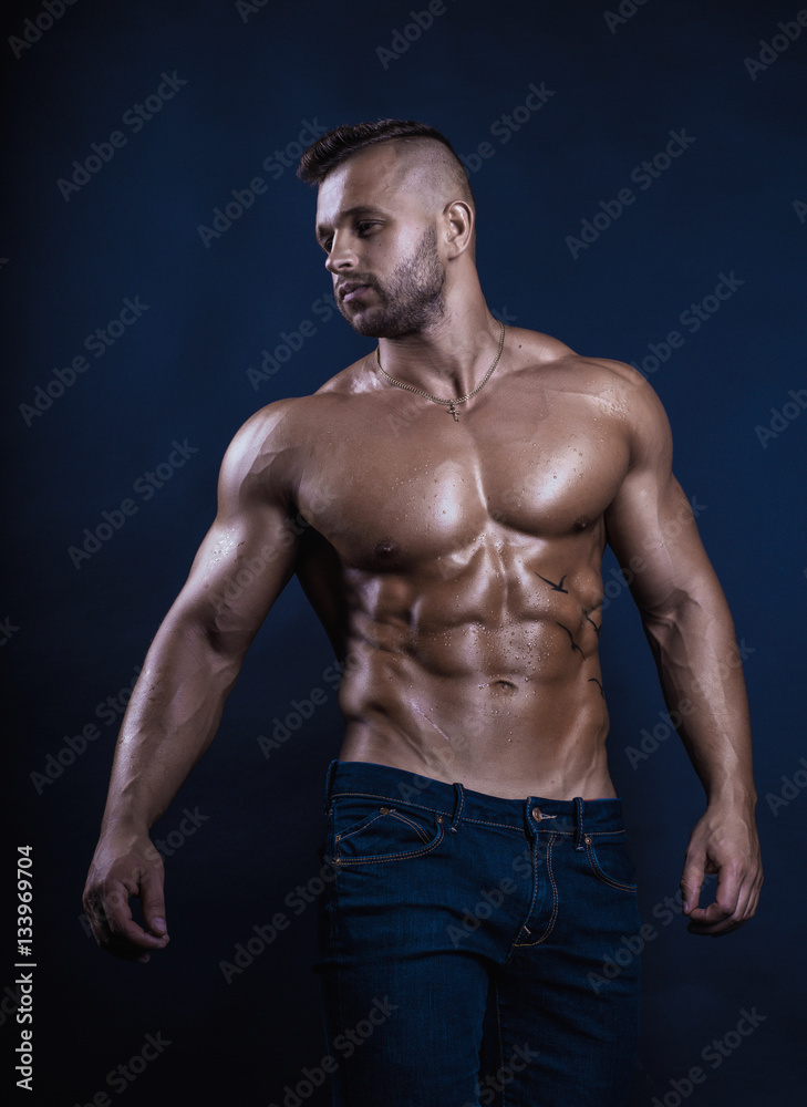 Handsome muscular bodybuilder posing over dark background