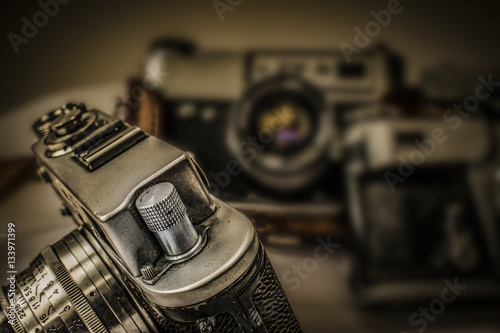 Close up view of old Russian analog film camera with vintage look. On the camera, there can be seen film rewind crank and flash hot shoe buttons. In background is another old camera with lens
