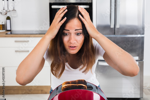 Frustrated Woman Looking At Burnt Toast In Toaster