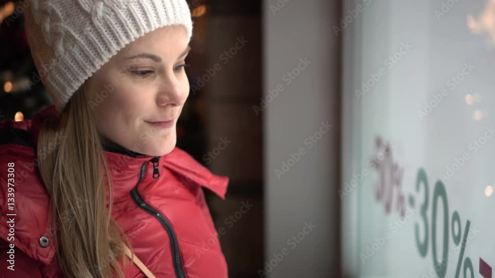 Beautiful attractive young woman looking at shop window. Red winter coat. Sales signs. Evening night. Beautiful attractive young woman looking at shop window. Red winter coat. Sales signs. Evening night.