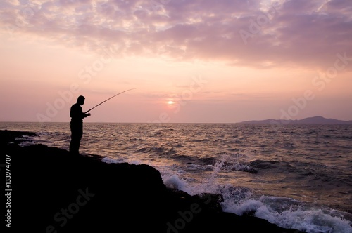 Silhouette of man fishing on the stone at seaside