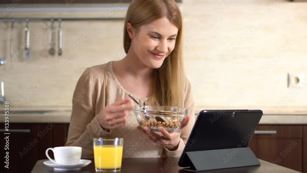 Beautiful young attractive woman having cornflakes for breakfast and using her tablet. Cup of coffee Beautiful young attractive woman having cornflakes for breakfast and using her tablet. Cup of coffee
