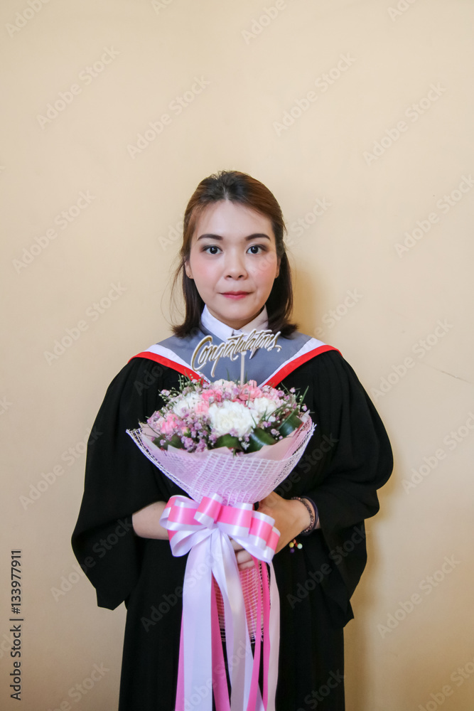 Asian student in black graduation gown holding bouquet with yellow background. Asian student in black graduation gown holding bouquet with yellow background.