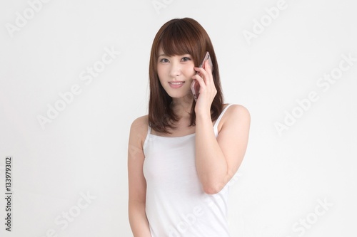 若い女性が、スマートフォンを操作しています。この画像の背景は白です。