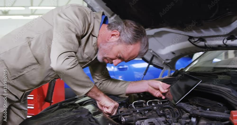 Mechanic using digital tablet while servicing a car engine Mechanic using digital tablet while servicing a car engine
