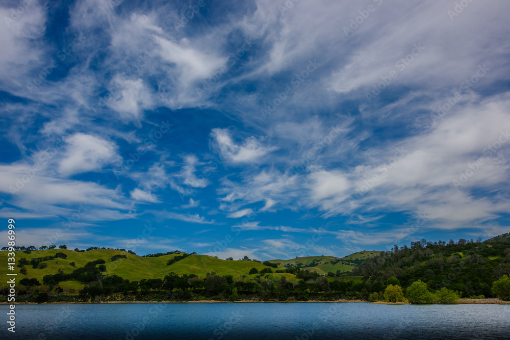 White clouds on blue sky over green hills and lake