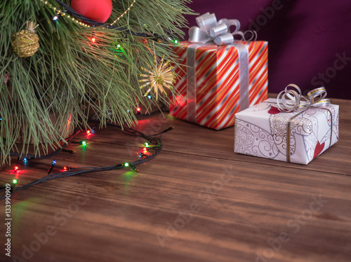 Green Christmas tree decorated with toys and garland with led lights. Boxes with gifts. Christmas present in boxes at wooden table. Green fir tree with toys and gifts under the tree.