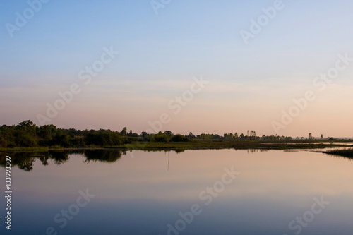 The sky in orange and blue shades is reflected on the water of the river. © THEGOT