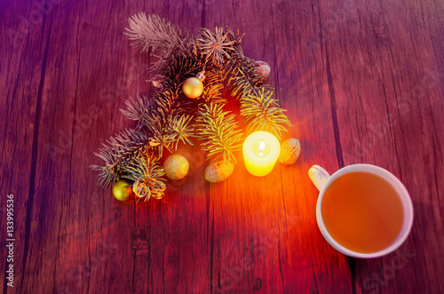 Cup of hot tea on a decorated table with candle, nut and pine trees on a winter evening. on wood background.