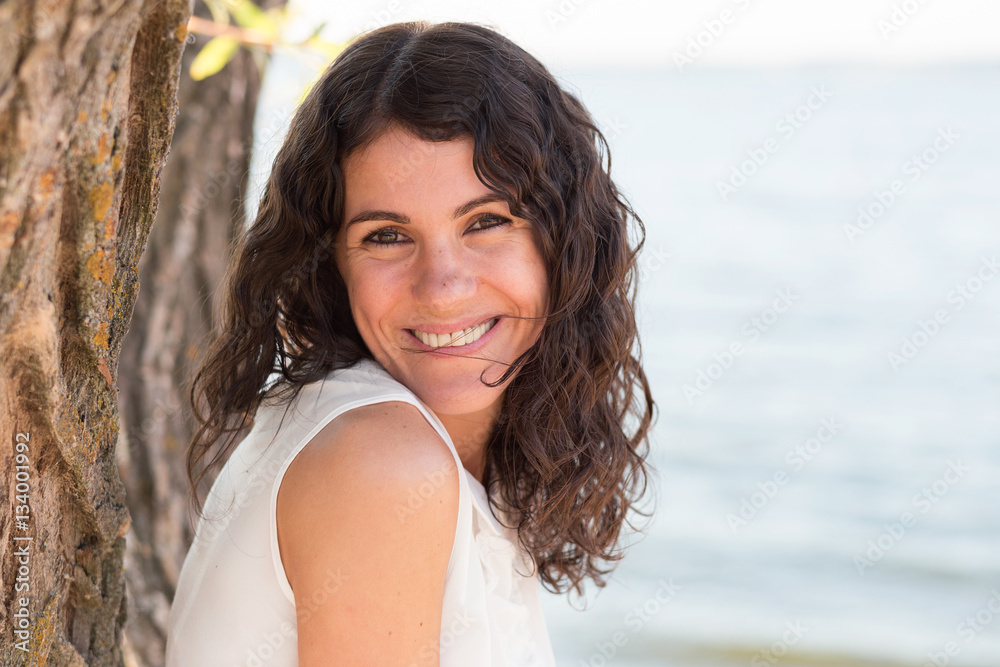 Portrait of a beautiful young happy woman with long curly hair looking at you on nature in summer Portrait of a beautiful young happy woman with long curly hair looking at you on nature in summer