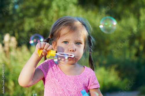 The girl in the pink dress 3 years and two braids enjoys life  inflating bubbles.
