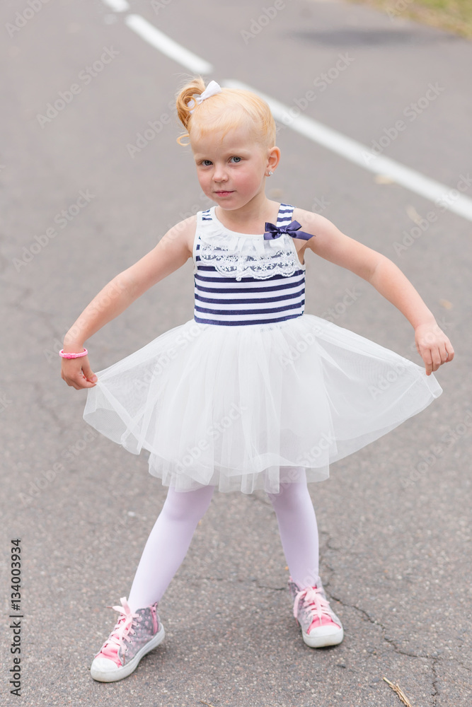 Fototapeta premium A cute little girl in a beautiful dress and sneakers playing on