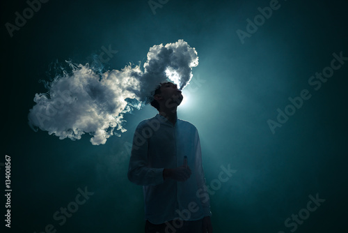 The man smoke an electrical cigarette on the dark background