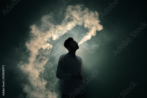 Canvas Print The man smoke an electronic cigarette on the dark background