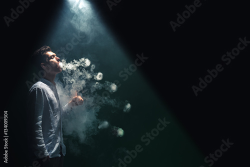 The man smoke an electronic cigarette with a ring and on the dark background