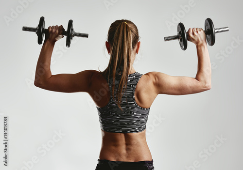 Studio portrait of young sporty female holding dumbbells. Concept of sport, fitness and wellness. 