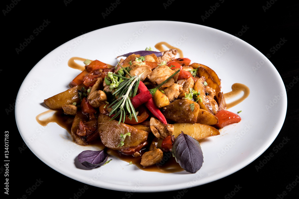 Fried potatos with vegetables and pork in white plate. Isolated on black background