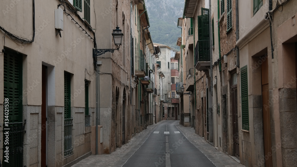 empty narrow street in Soller Mallorca with typical historic houses on both sides and mountains in far distant background
