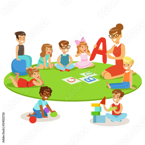 Young Children Learning Alphabet And Playing In Nursery School With Teacher Sitting And Laying On The Floor