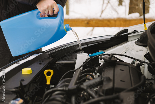 Car maintenance. Man pouring car winter windshield washer fluid outdoor. Closeup image taken outdoors.