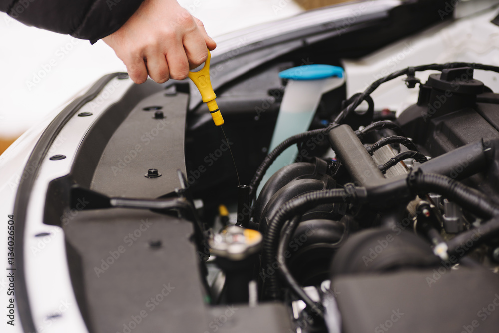Car maintenance before winter. Man checking oil level in his car using dipstick. Outdoor closeup photograph Car maintenance before winter. Man checking oil level in his car using dipstick. Outdoor closeup photograph