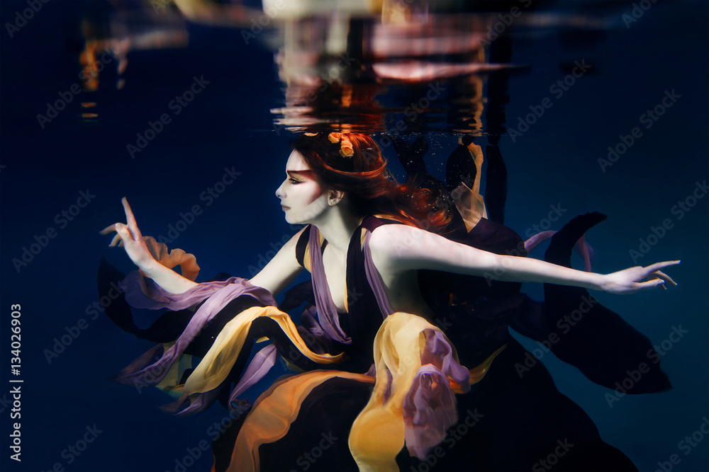Fototapeta dziewczyna w kolorowe ubrania na ciemnym tle pływanie pod wodą