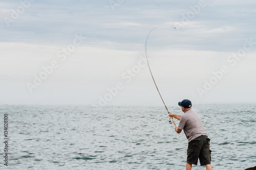 Man fishing on a breakwater of the Atlantic Ocean with a boat in