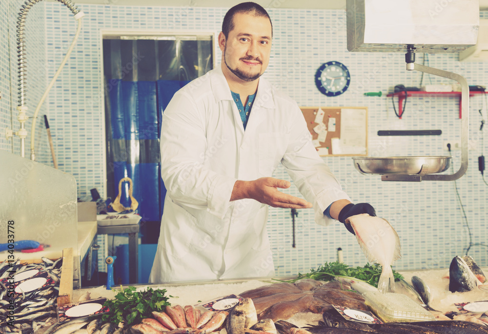 Man in glove behind counter shows fish in his hand