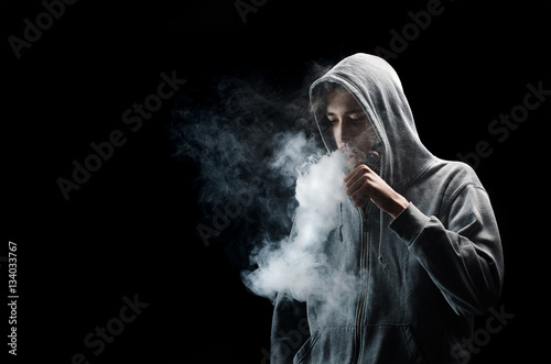One man in the hood vaping e-cigarette and blowing a cloud.