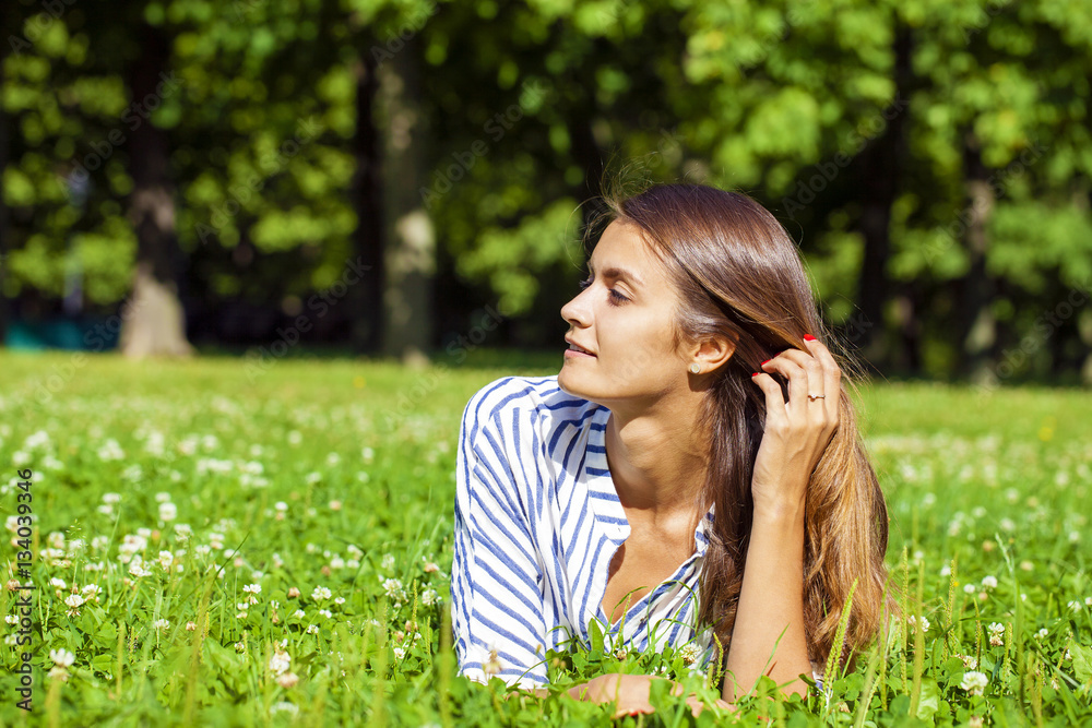 Attractive young brunette woman lying on green grass field at su Attractive young brunette woman lying on green grass field at su