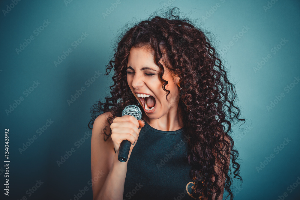 Business woman screaming / talking in microphone. Funny photo of young casual beautiful business woman lady holding microphone. Asian Caucasian female model isolated on blue indoor background. Business woman screaming / talking in microphone. Funny photo of young casual beautiful business woman lady holding microphone. Asian Caucasian female model isolated on blue indoor background.