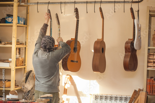 Serious professional guitar-maker takes with unfinished guitar at workshop