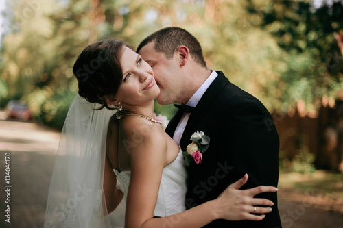 Fotografie Elegant young happy wedding couple is sitting at green grass on