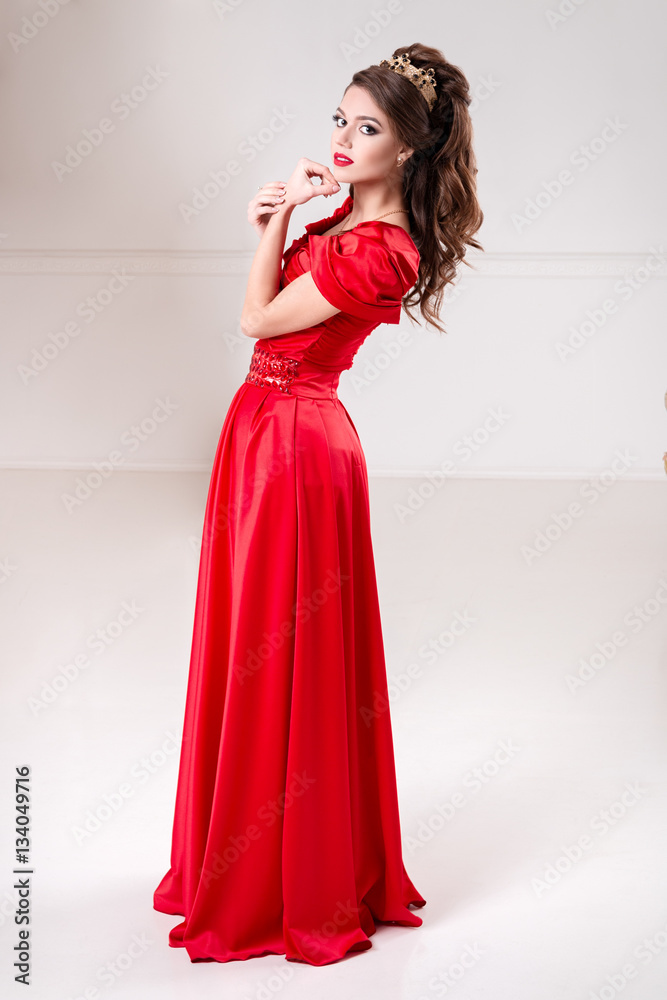 elegant woman in a long red dress is standing in a white room elegant woman in a long red dress is standing in a white room